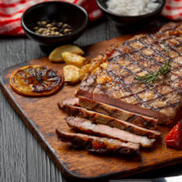 Grilled beef steak on the dark wooden background.