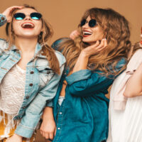 Three young beautiful smiling hipster girls in trendy summer casual jeans clothes. Sexy carefree women posing near golden wall. Positive models going crazy in sunglasses